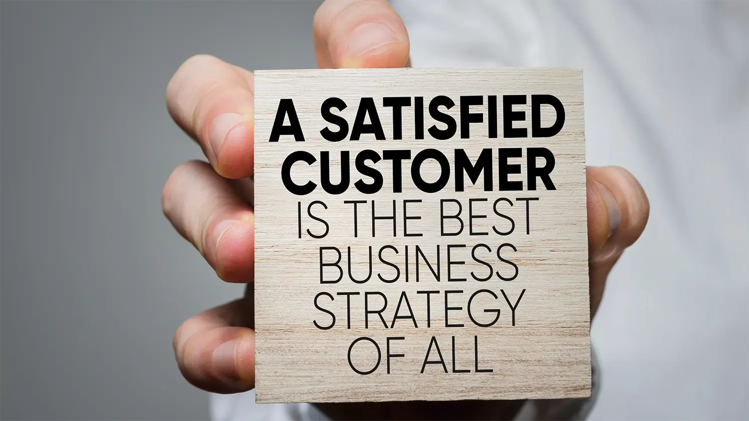 Image of a Hand Holding a Block with the Phrase &quot;A Satisfied Customer is the Best Business Strategy of All&quot;